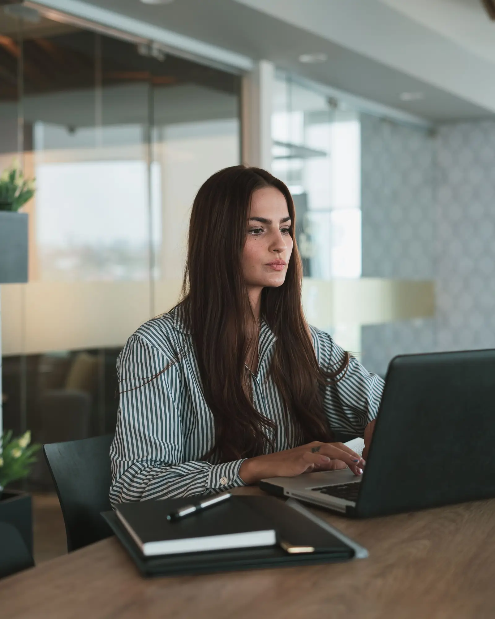 A woman works with focus on a laptop at a desk in a modern office.
