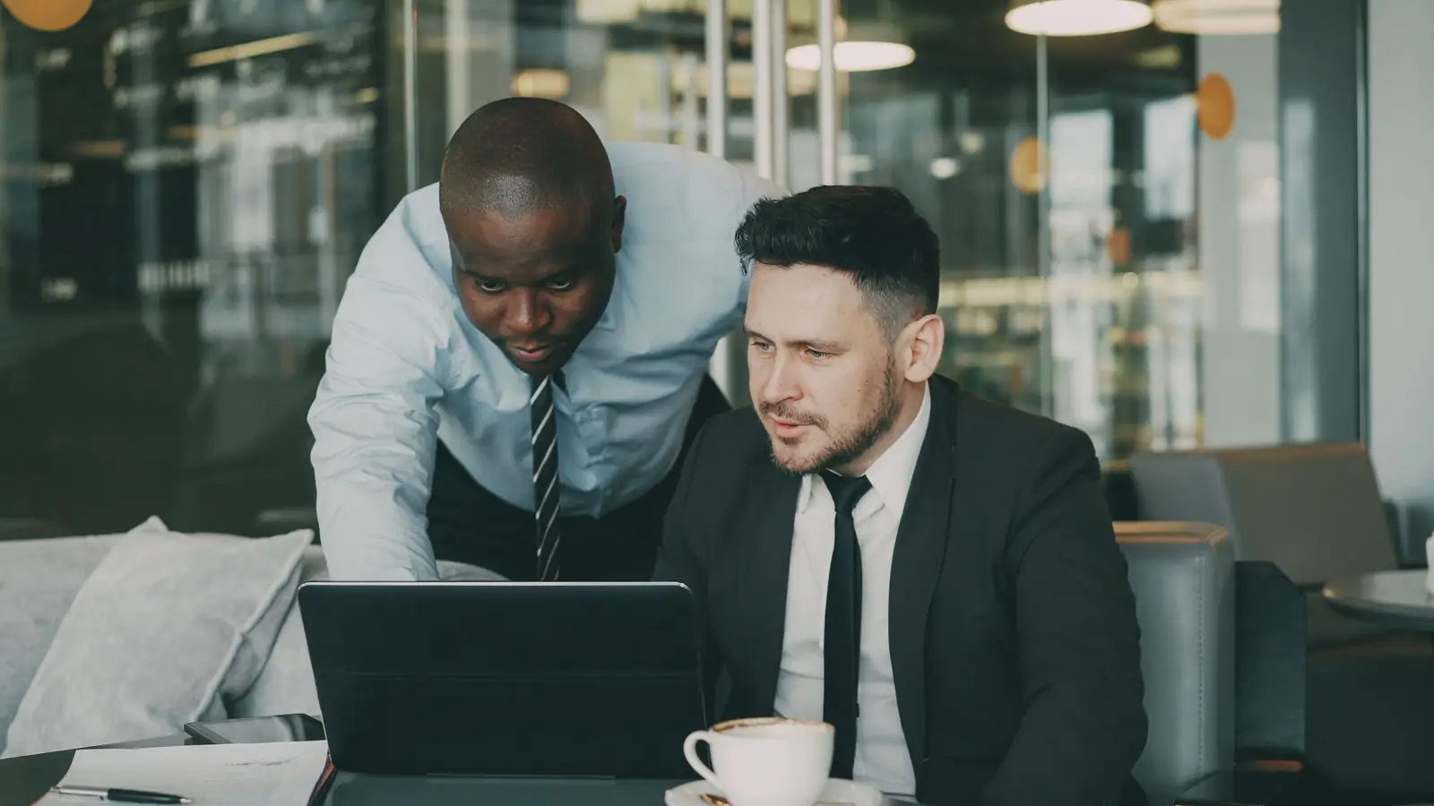 Two colleagues talk through work together at a laptop in a modern office.
