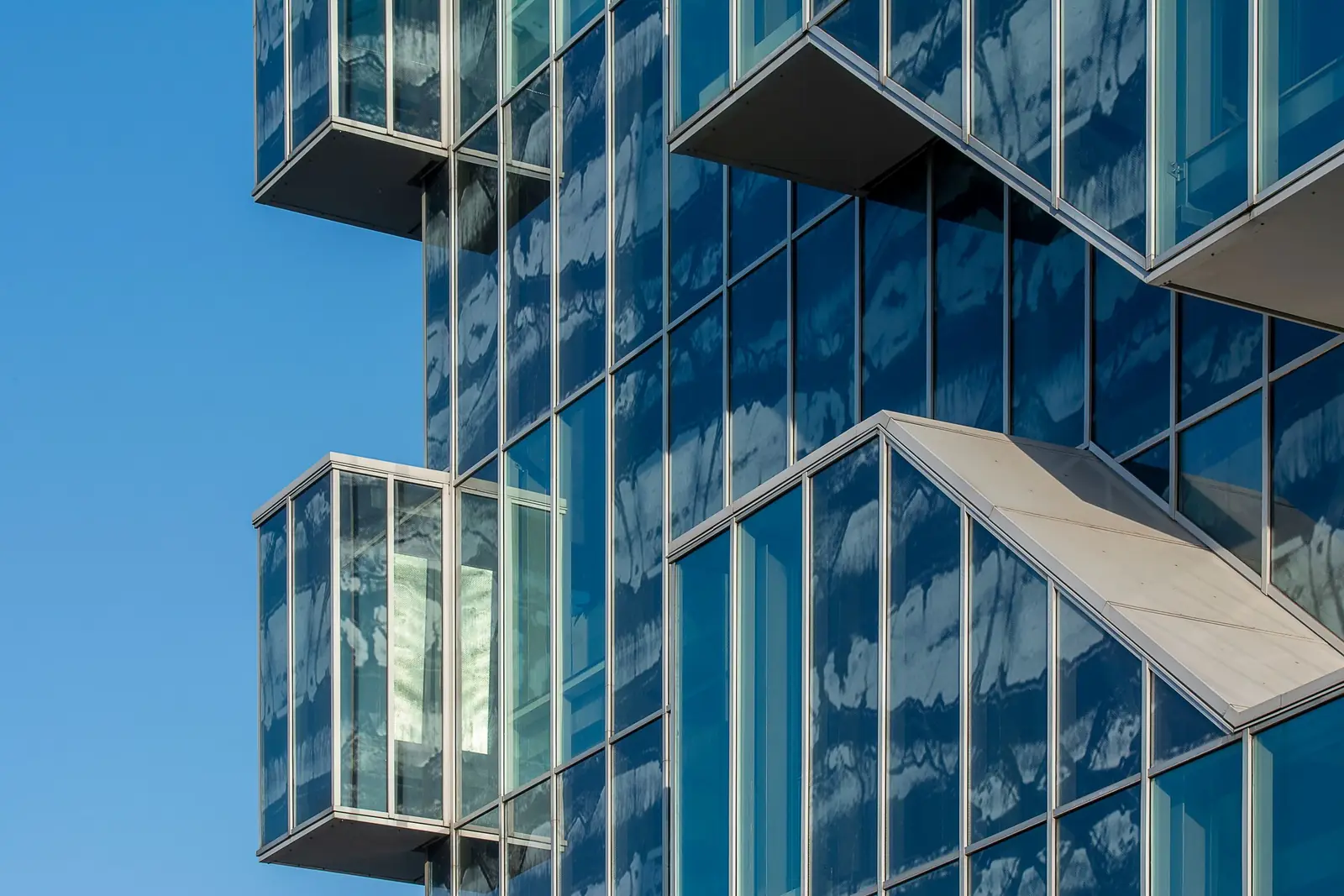 Glasfassade eines modernen Bürogebäudes, in der sich Himmel und Wolken spiegeln.